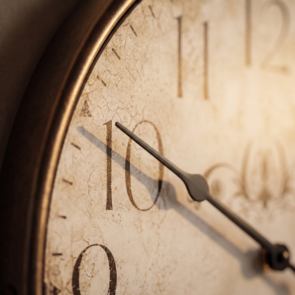 Close-up of a round wall clock with a distressed cream face, dark numerals, and dark hands, framed by a warm metallic bronze rim.