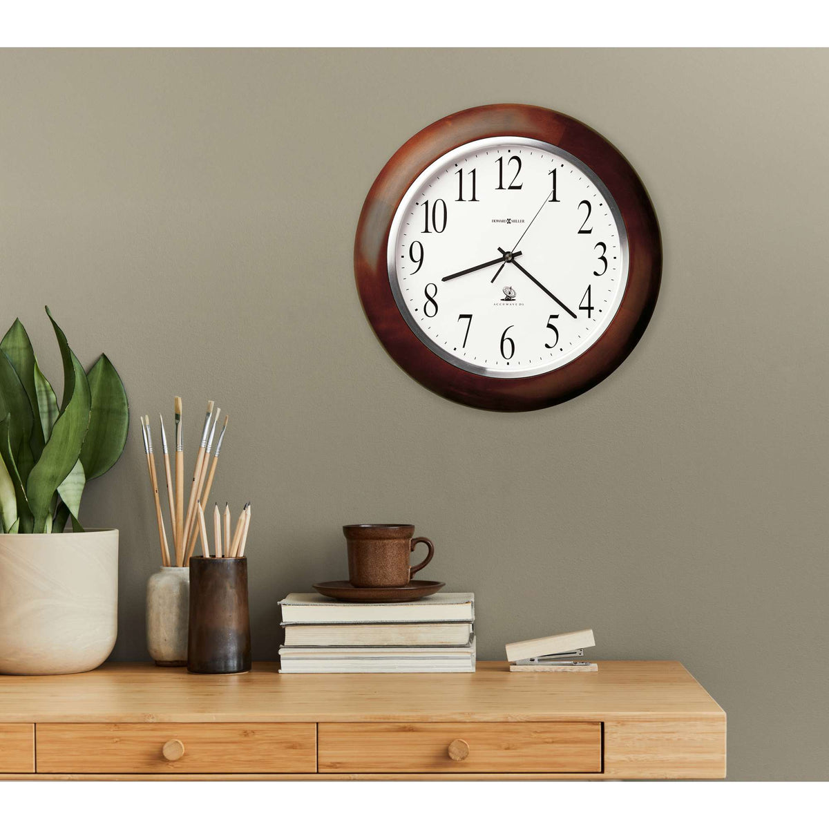 Wall-mounted clock above a wooden dresser with a plant and coffee cup