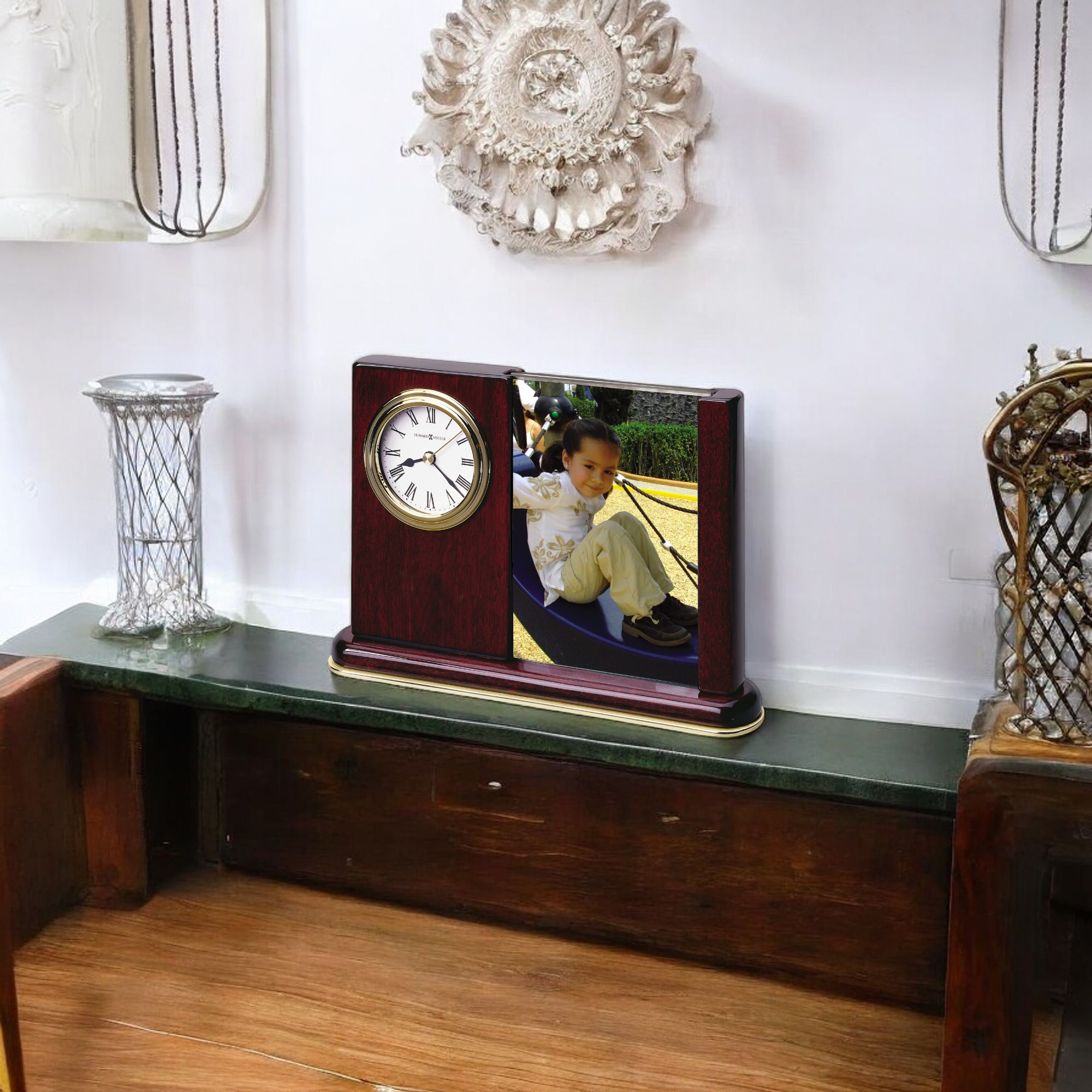 A clock on a wooden shelf with a framed photo of a child playing.