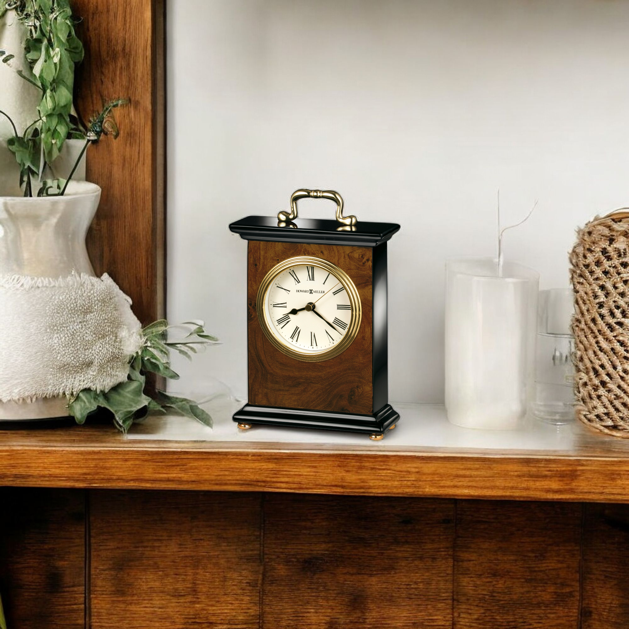 A wooden clock with a white face and gold accents on a shelf with greenery and decorative items.