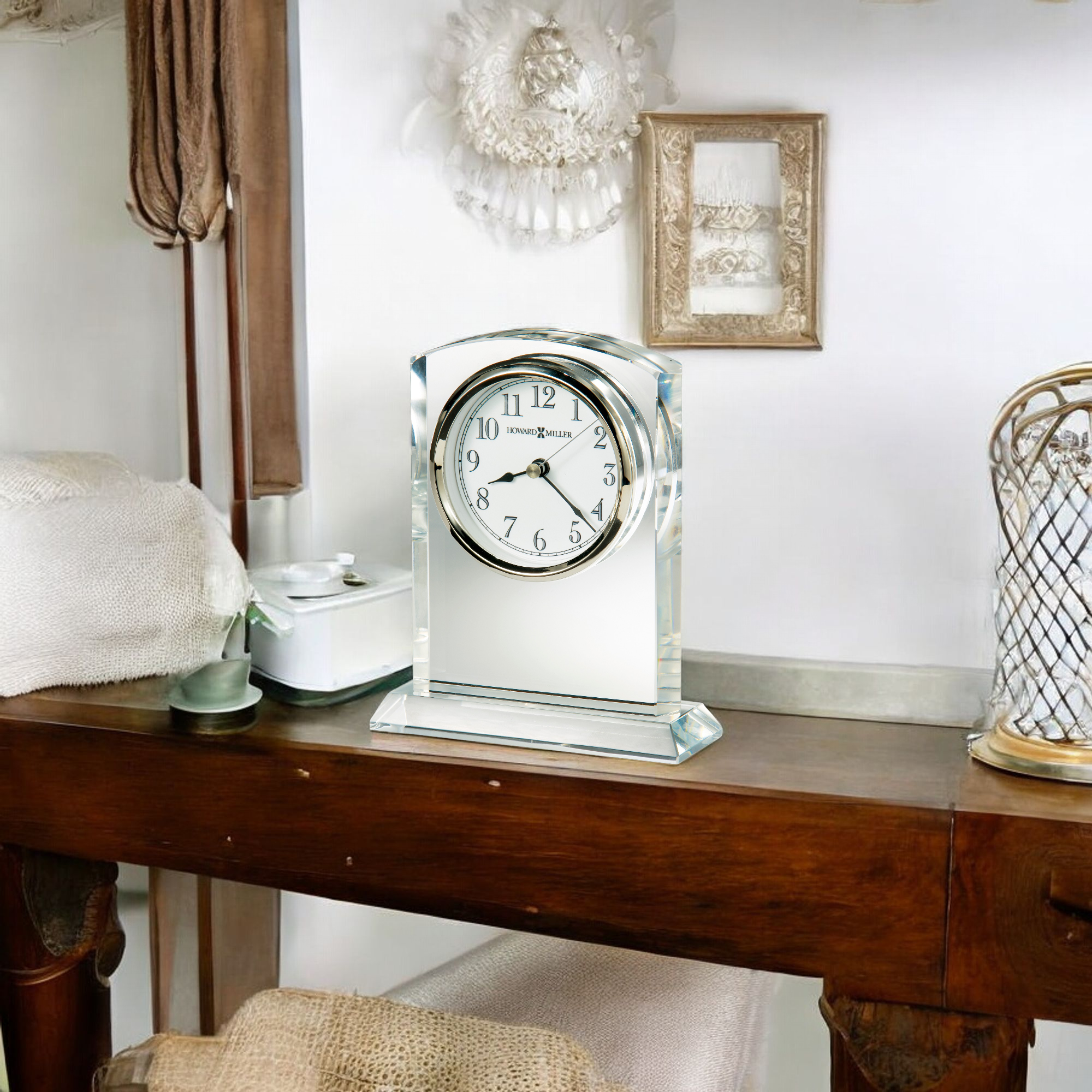 A vintage-style clock on a wooden table with soft textiles and decor in a cozy setting.