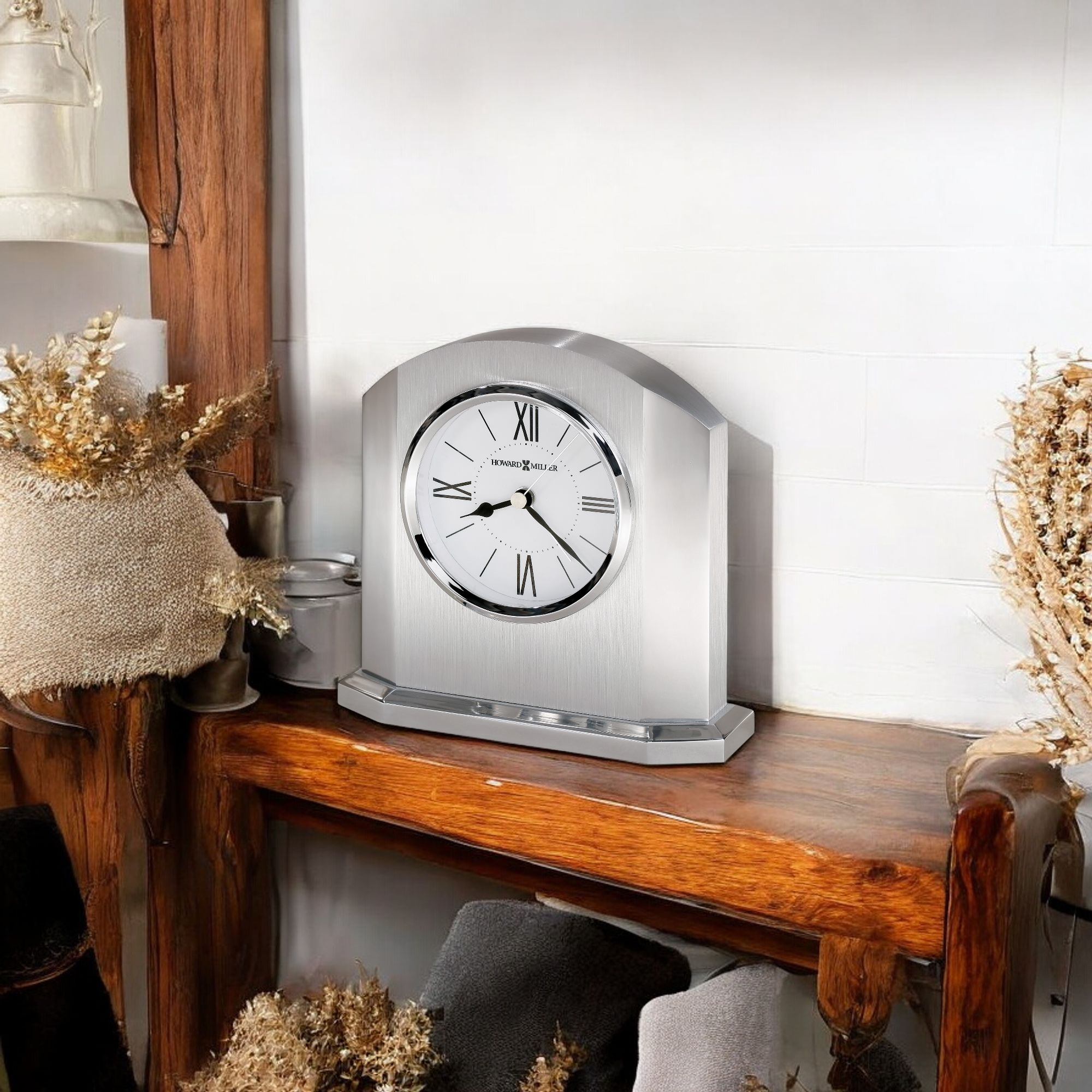 A decorative silver clock on a wooden shelf with dried flowers.