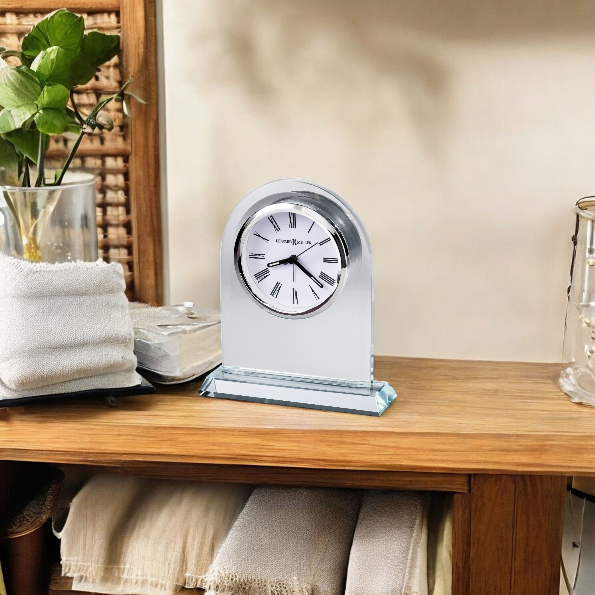A stylish silver clock on a wooden shelf adorned with decorative items.