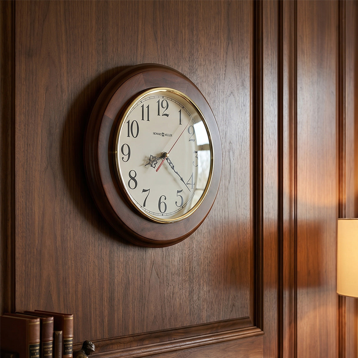 Wooden wall clock on a wooden wall with books and a lamp in the background