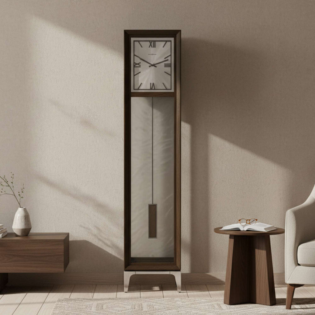 A modern grandfather clock with a square face and pendulum, positioned next to a side table and chair in a softly lit room.
