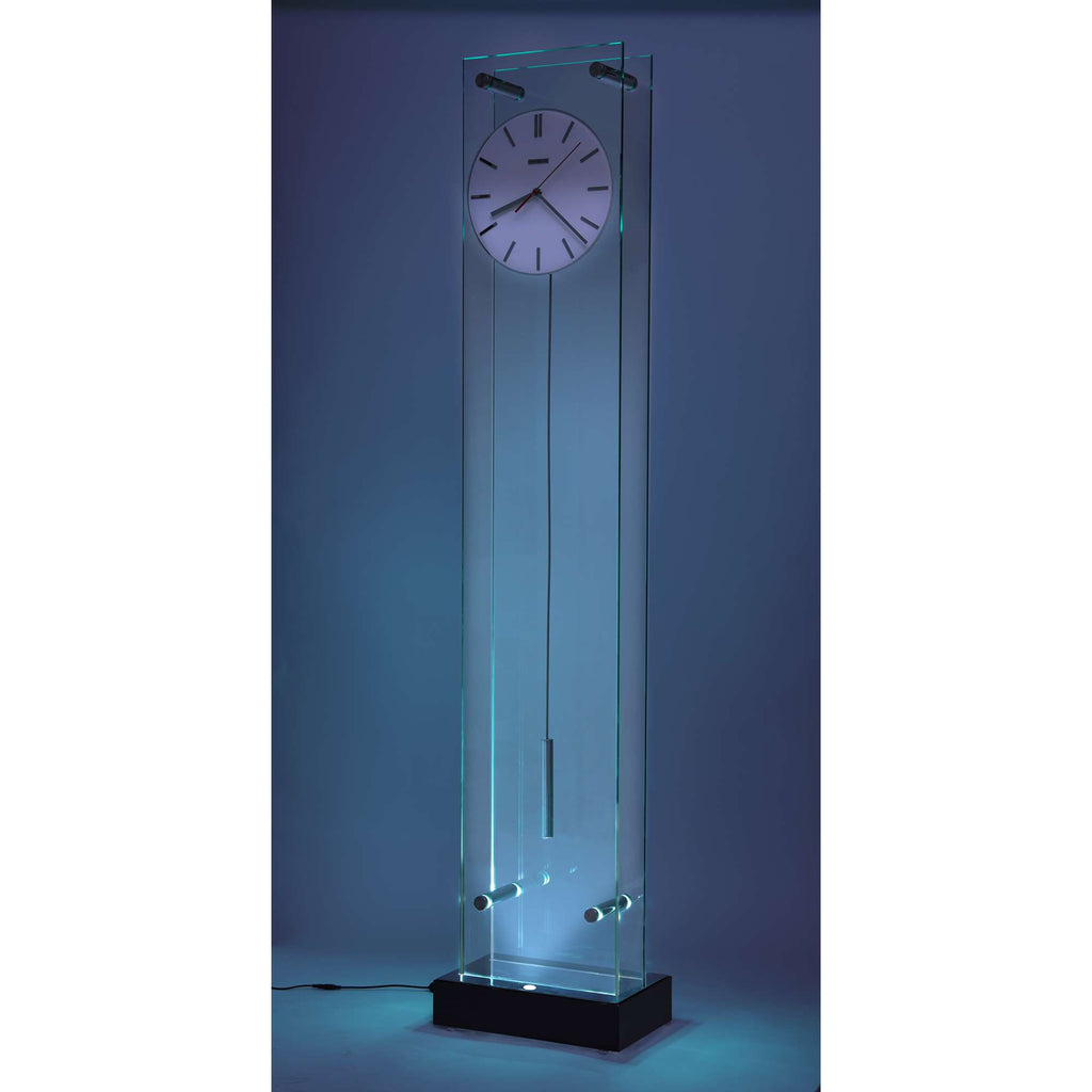 A modern, tall glass clock with a circular face, illuminated in blue.