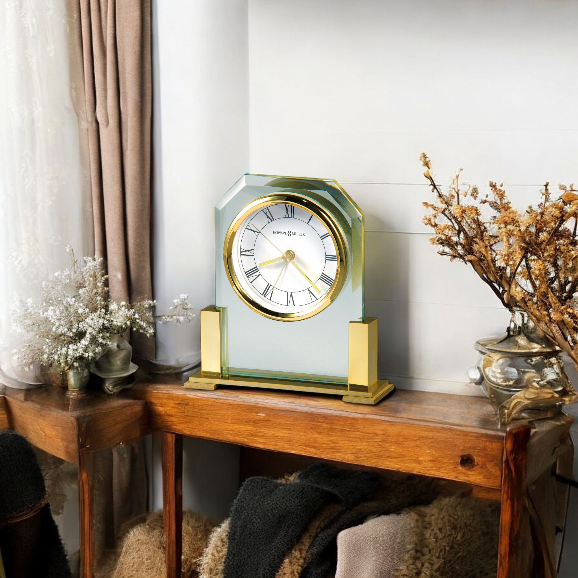 A decorative clock displayed on a wooden console table with flowers and a cozy throw.