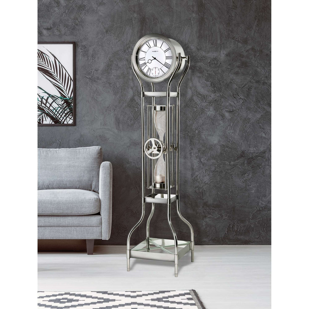 A stylish floor clock with a modern design, placed next to a gray sofa in a minimalist room.
