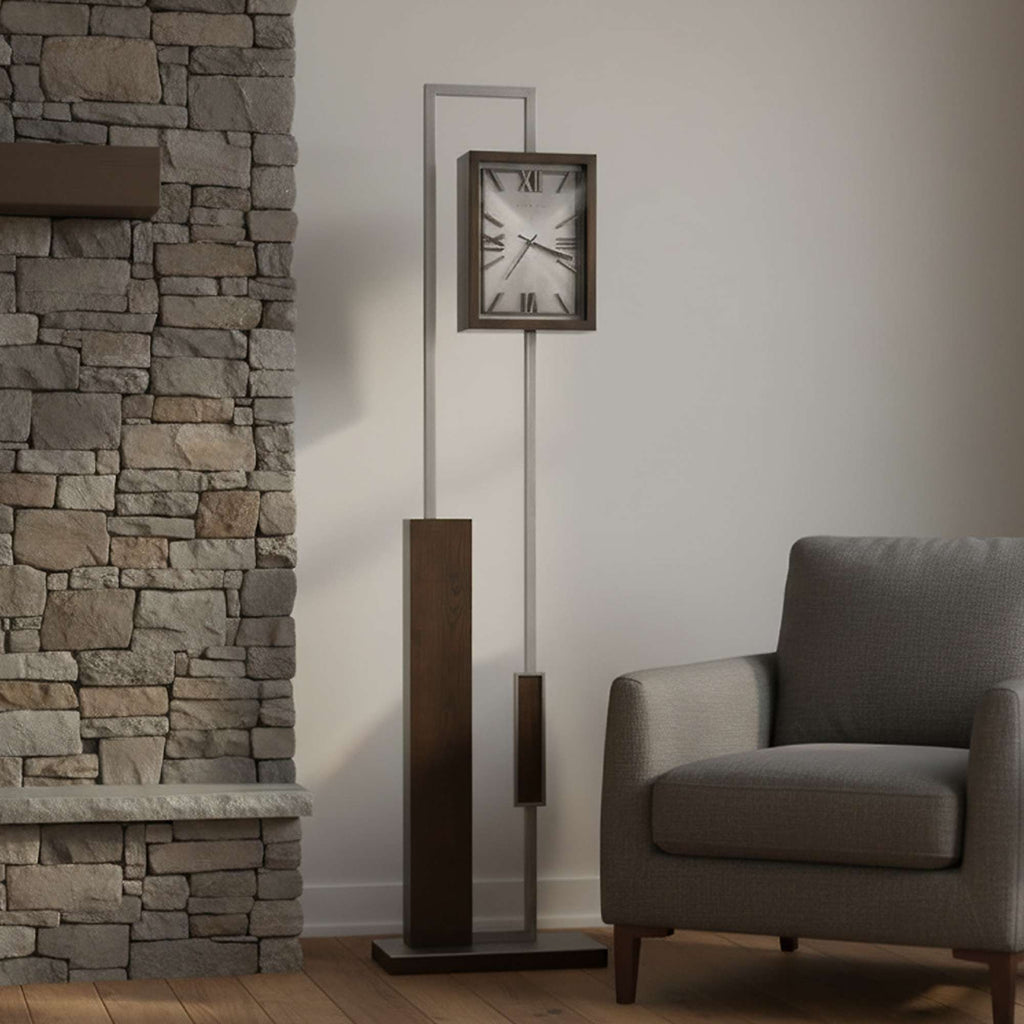Modern floor clock beside a grey armchair against a stone wall