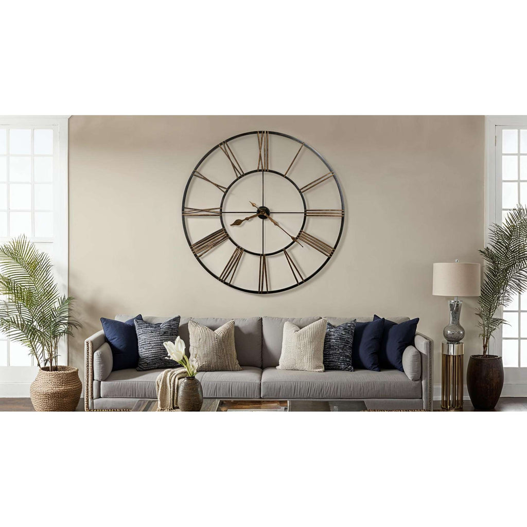A modern living room featuring a large wall clock above a stylish sofa with decorative pillows.
