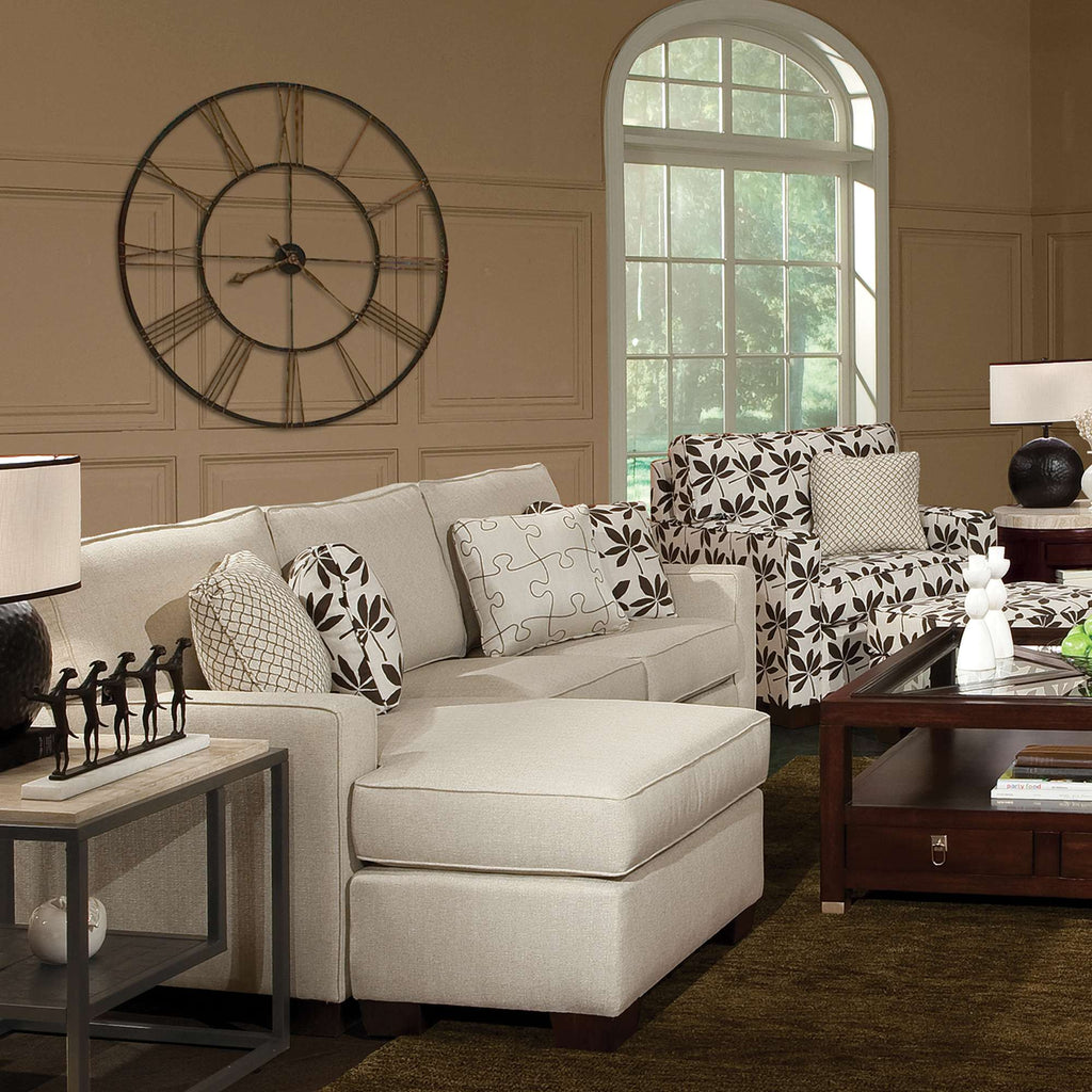 Modern living room with a beige sectional sofa, floral patterned armchairs, and a large wall clock.