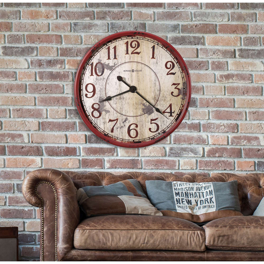 Vintage wall clock on a brick wall above a leather couch with patterned pillows.
