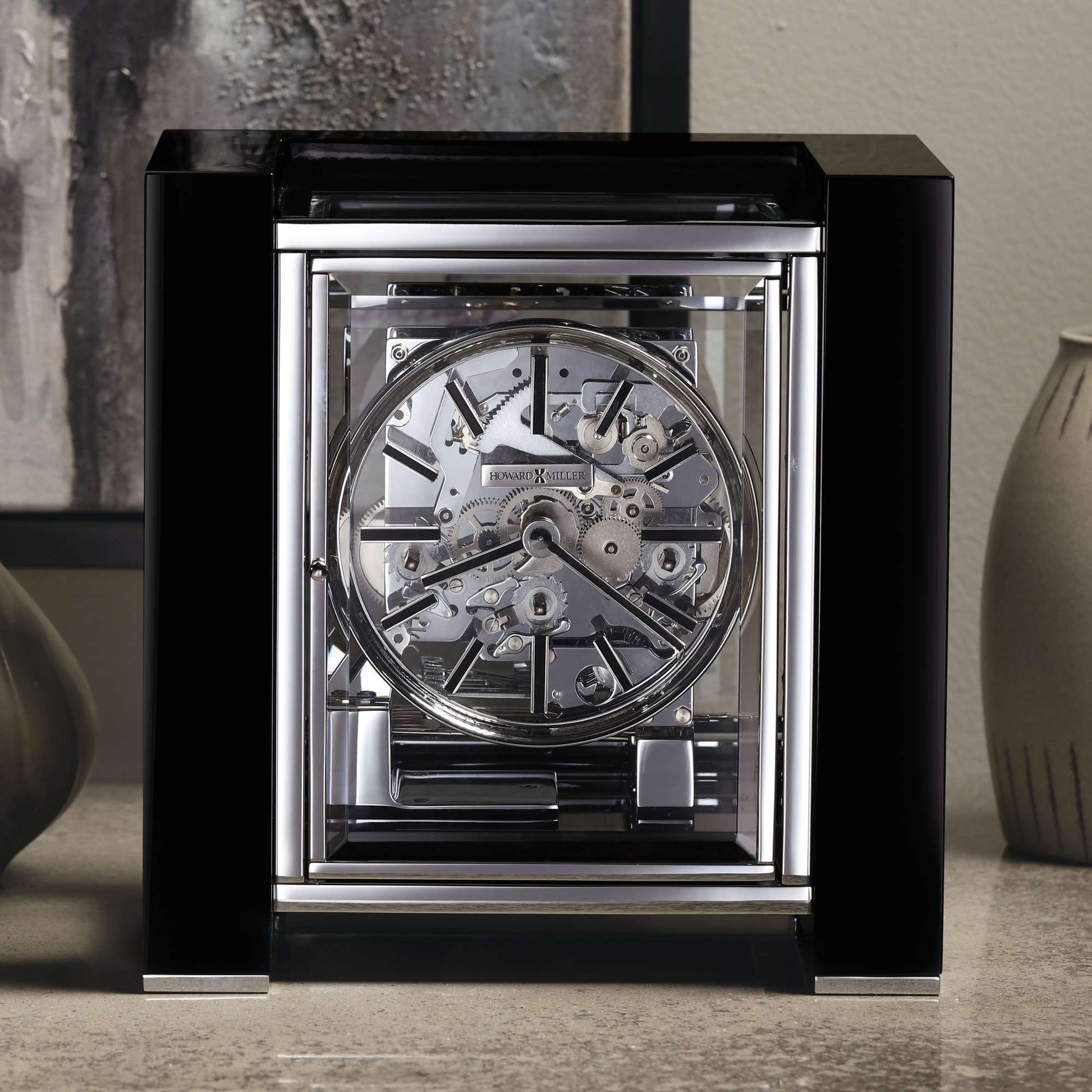 A modern, transparent clock showcased on a countertop with decorative vases in the background.