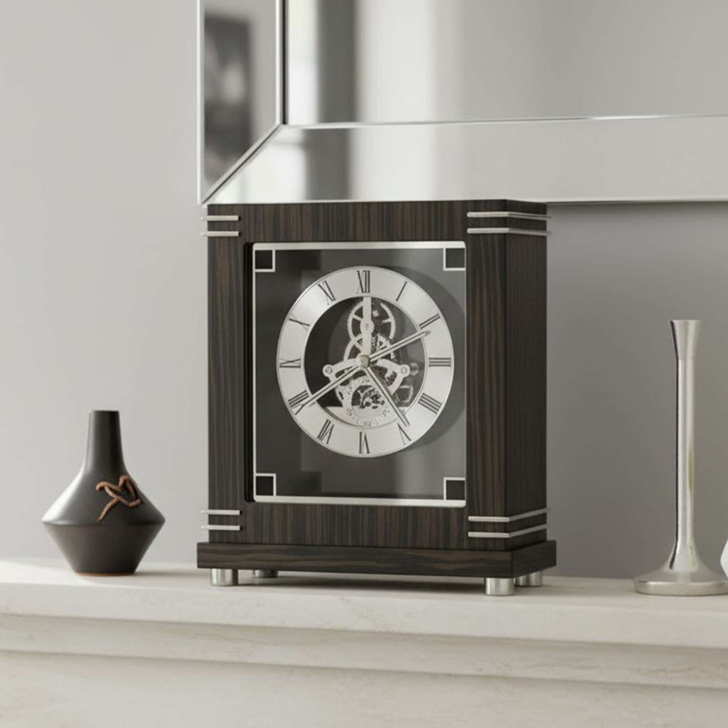 A stylish mantel clock with Roman numerals on a polished wood base, accompanied by a vase and a silver object.
