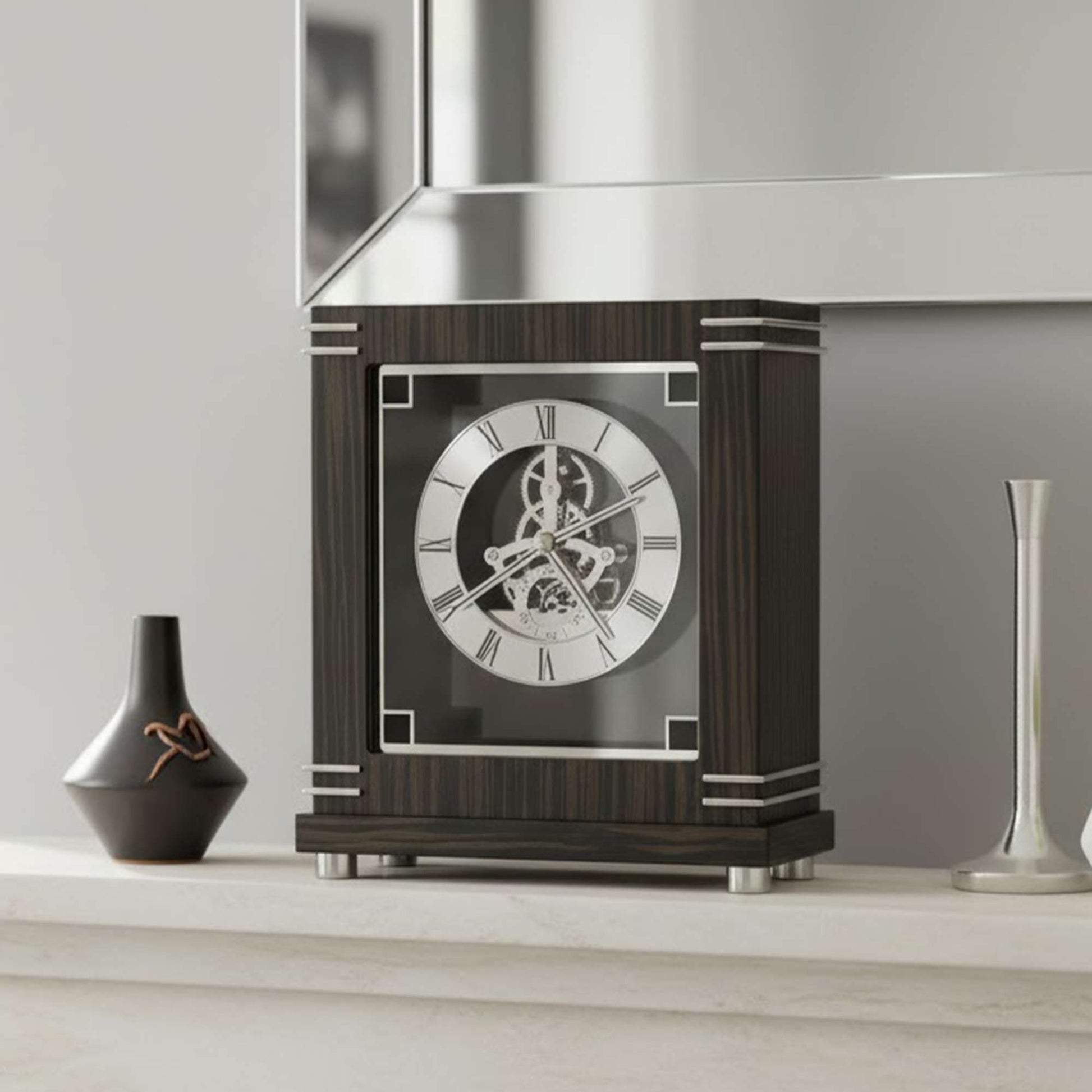A stylish mantel clock with Roman numerals on a polished wood base, accompanied by a vase and a silver object.