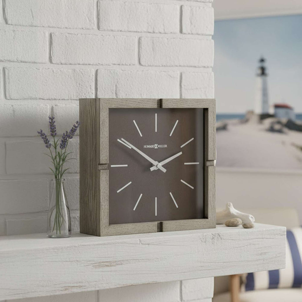 A contemporary square wall clock on a white shelf with lavender and a decorative object.