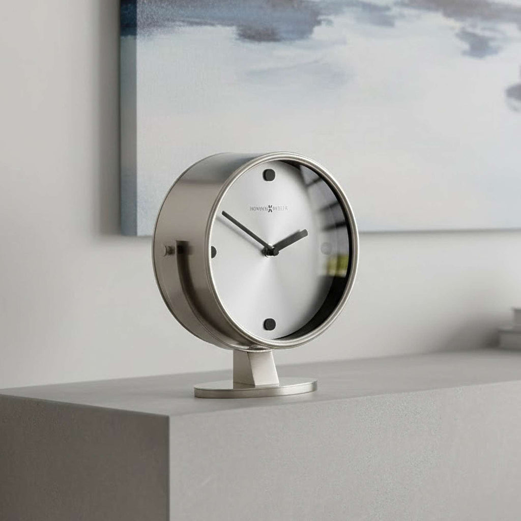 A modern, minimalist table clock with a sleek circular design on a flat surface.