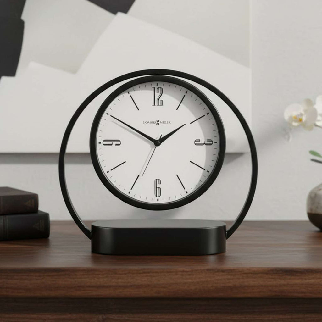 A modern black circular clock displayed on a wooden surface, featuring a white face with black numbers.