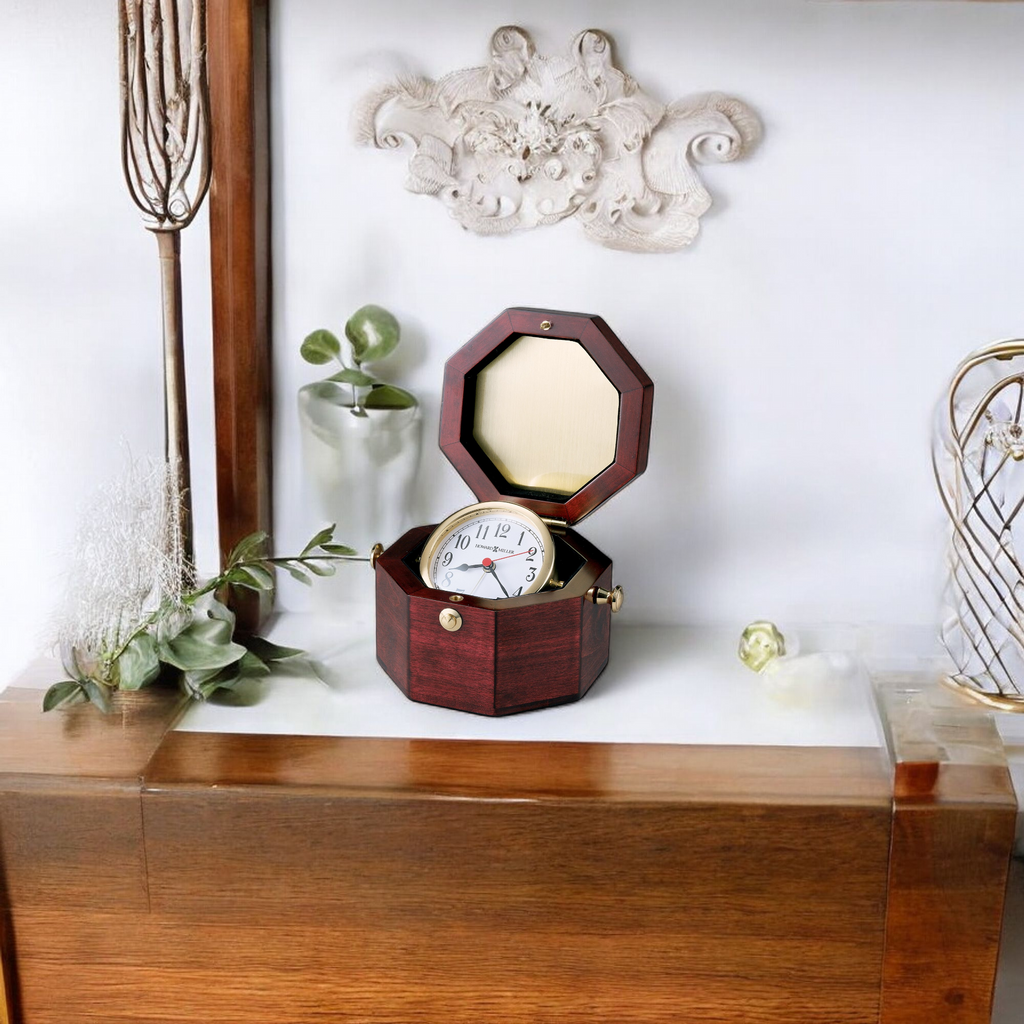 A wooden octagonal jewelry box with a mirror and clock, placed on a wooden surface beside decorative plants.