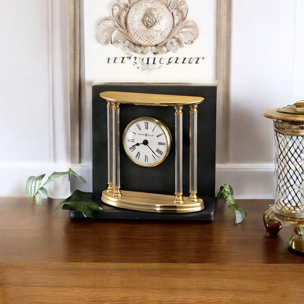 A decorative wall clock with a gold frame and clear columns, placed on a wooden surface.