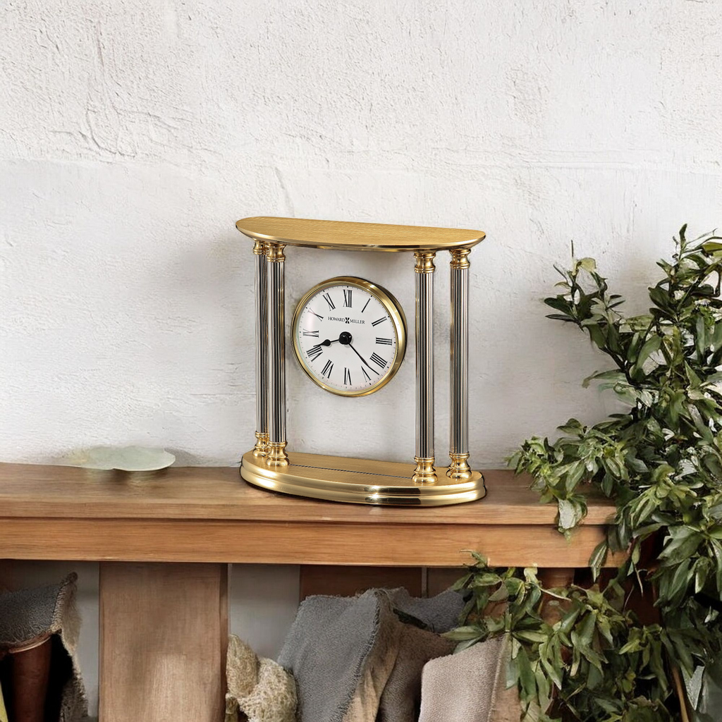 Elegant gold table clock with a white face and glass columns on a wooden shelf