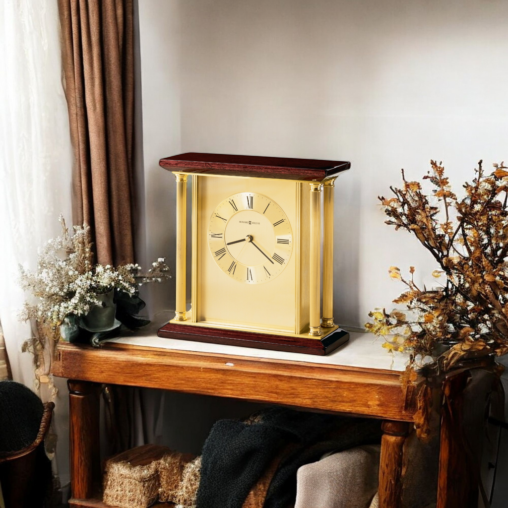 A gold and wood table clock displayed on a wooden table with decorative plants.