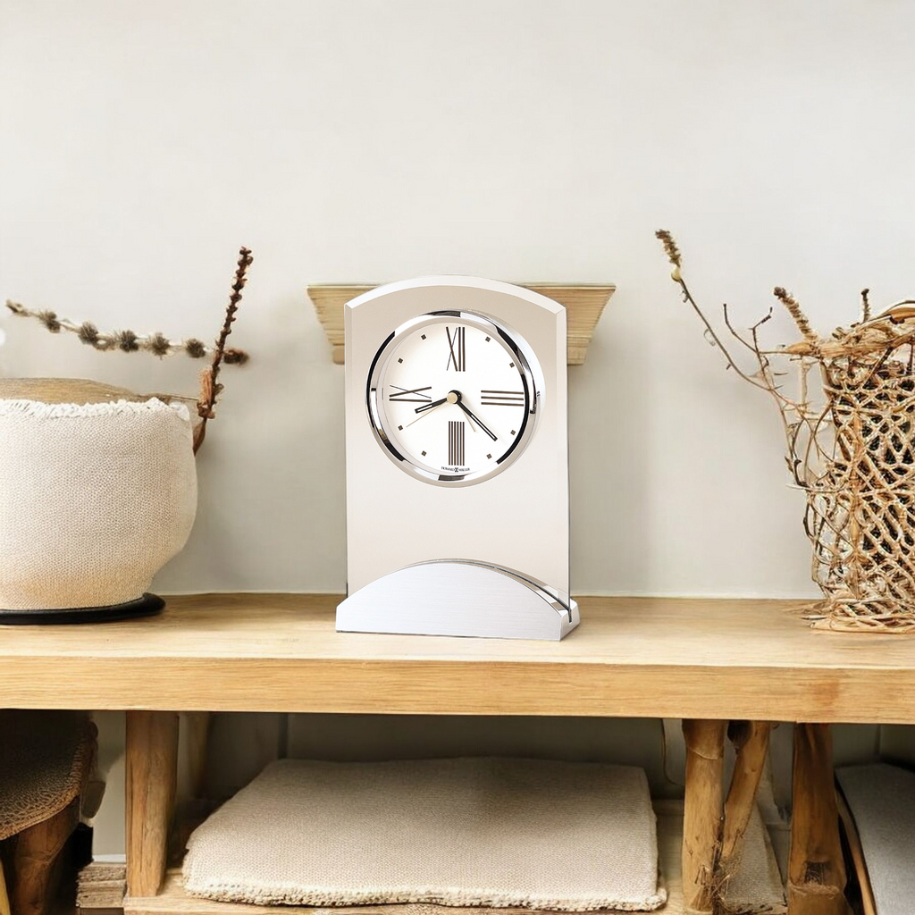 A modern clock displayed on a wooden shelf with decorative items.