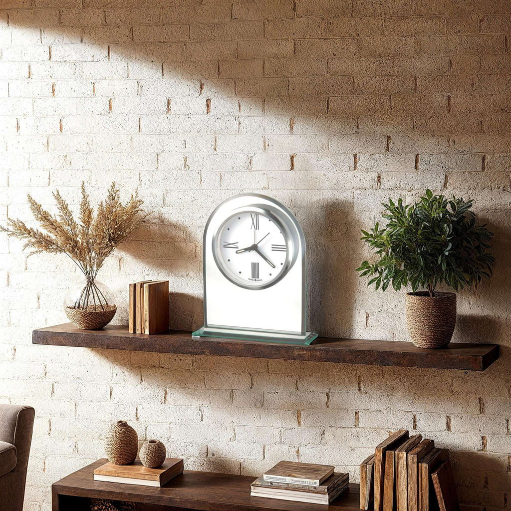 A modern clock displayed on a wooden shelf with decorative plants.