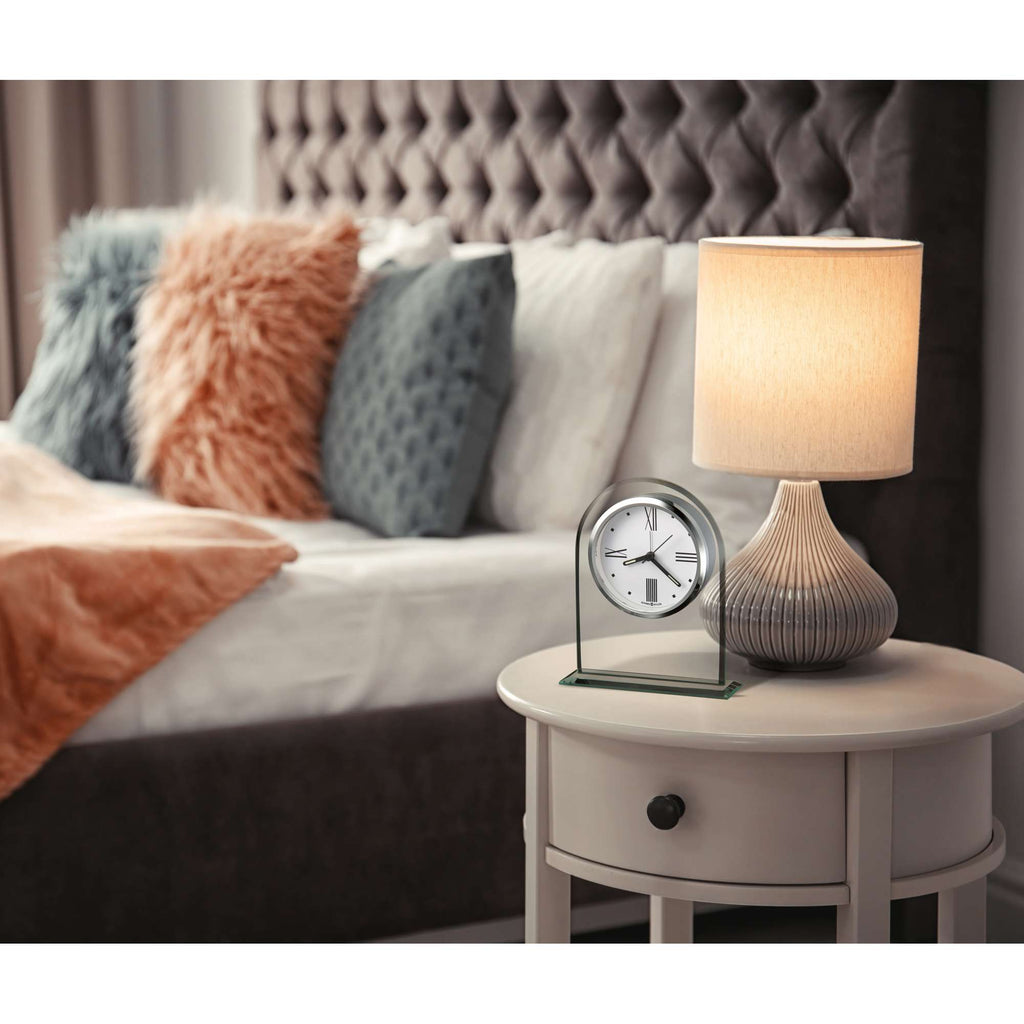 A cozy bedroom scene featuring a bedside table with a clock and lamp, plush pillows on the bed, and a soft throw blanket.