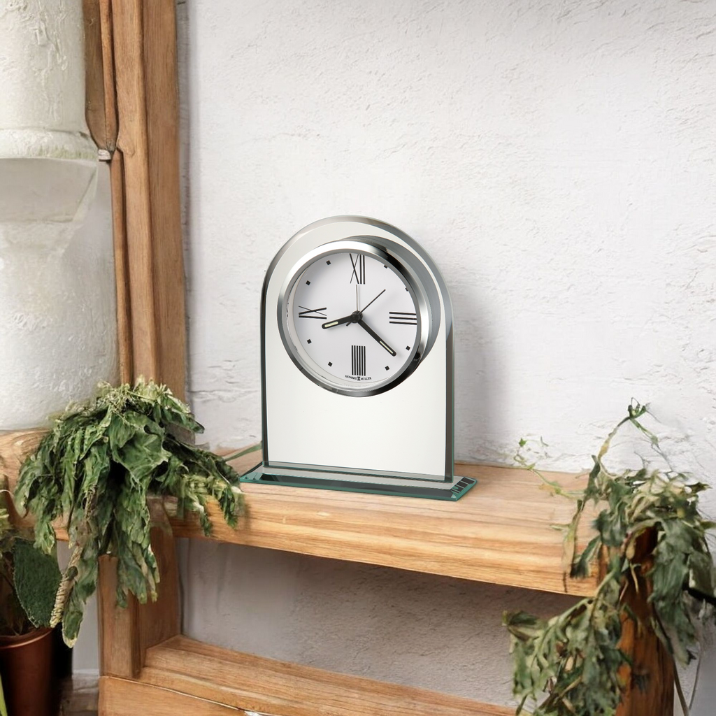 A modern clock displayed on a wooden shelf surrounded by greenery.