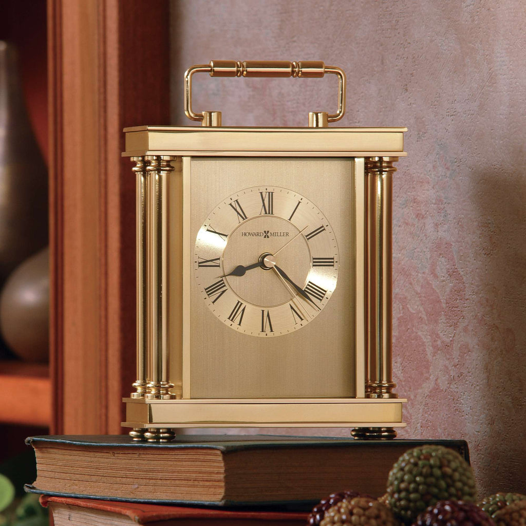 A vintage gold desk clock with Roman numerals, placed on a stack of books.