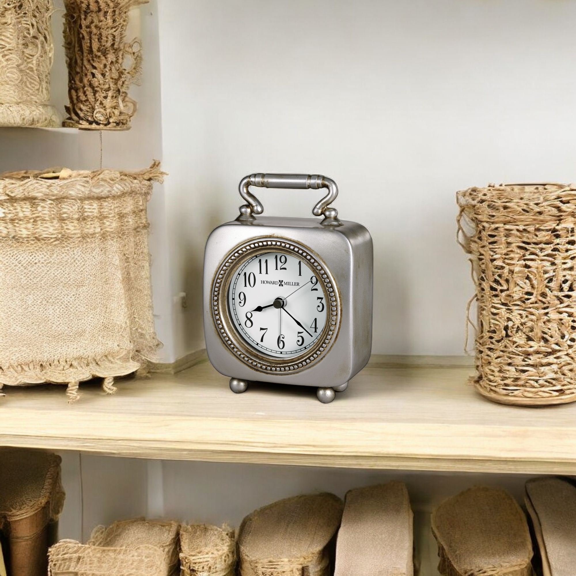 A vintage silver alarm clock on a wooden shelf surrounded by woven baskets.