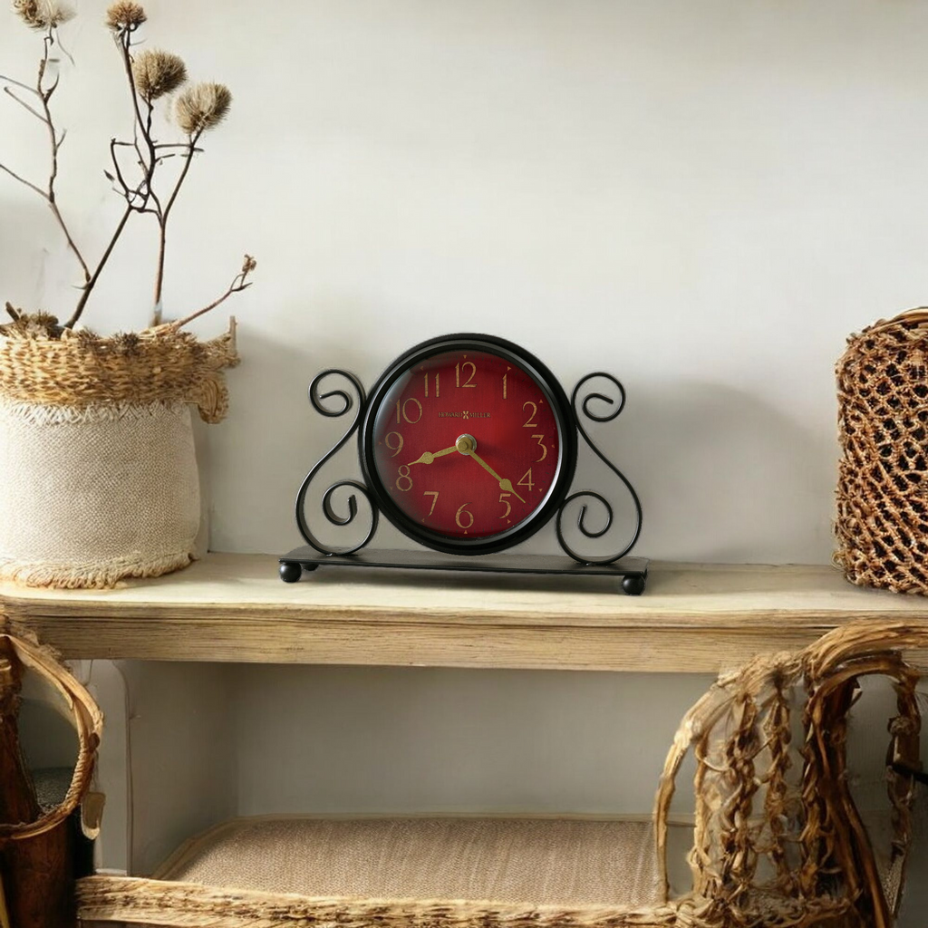 A decorative vintage clock with a red face and black frame, placed on a wooden shelf surrounded by woven baskets and dried flowers.