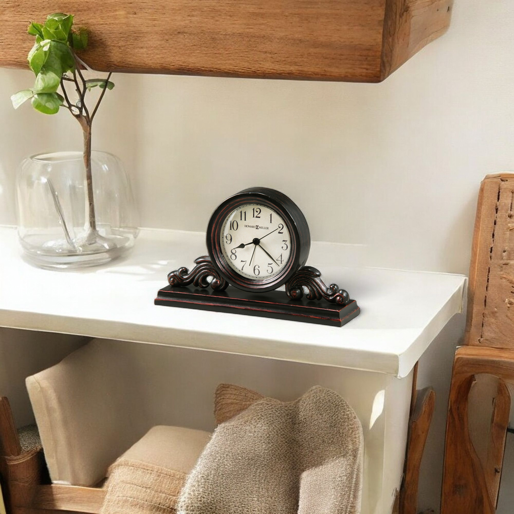 A decorative clock on a white shelf with a glass vase and soft textiles.