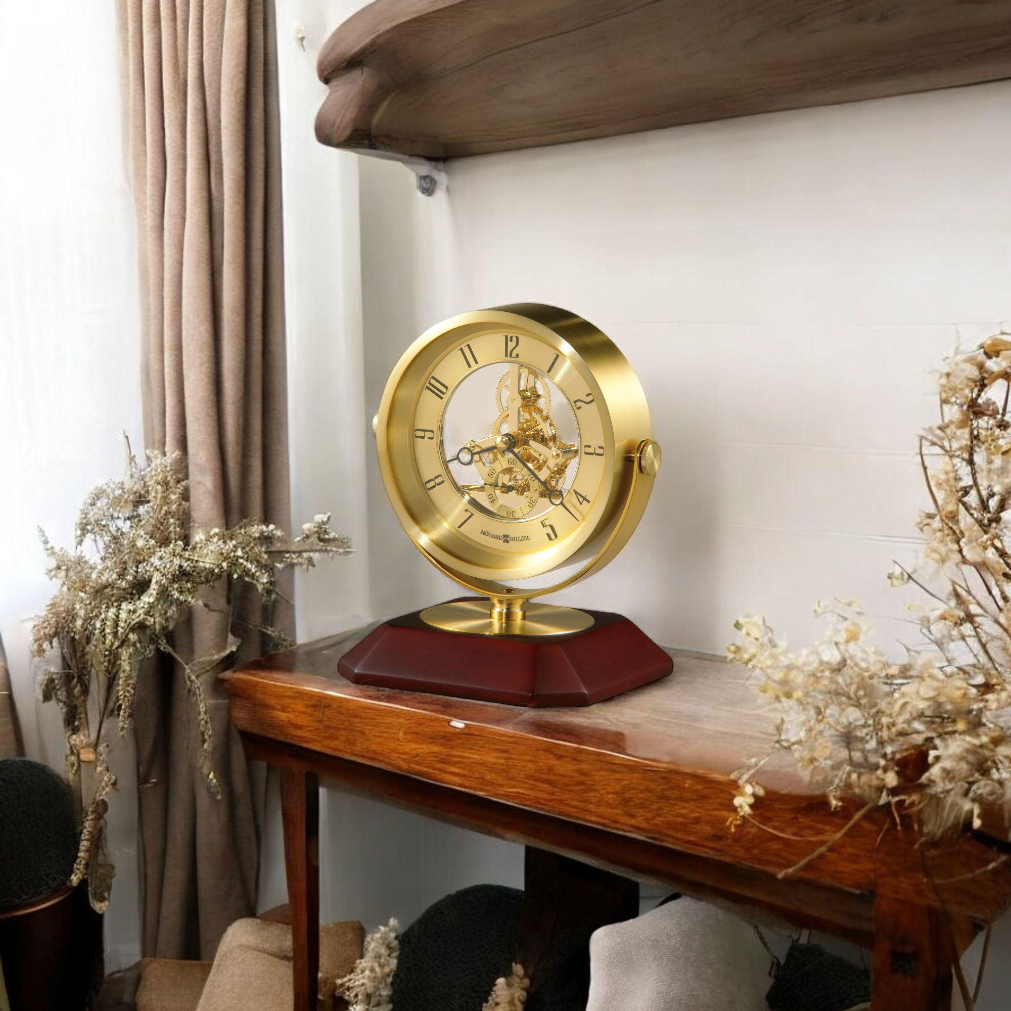 A decorative golden clock on a wooden table with dried flowers in the background.