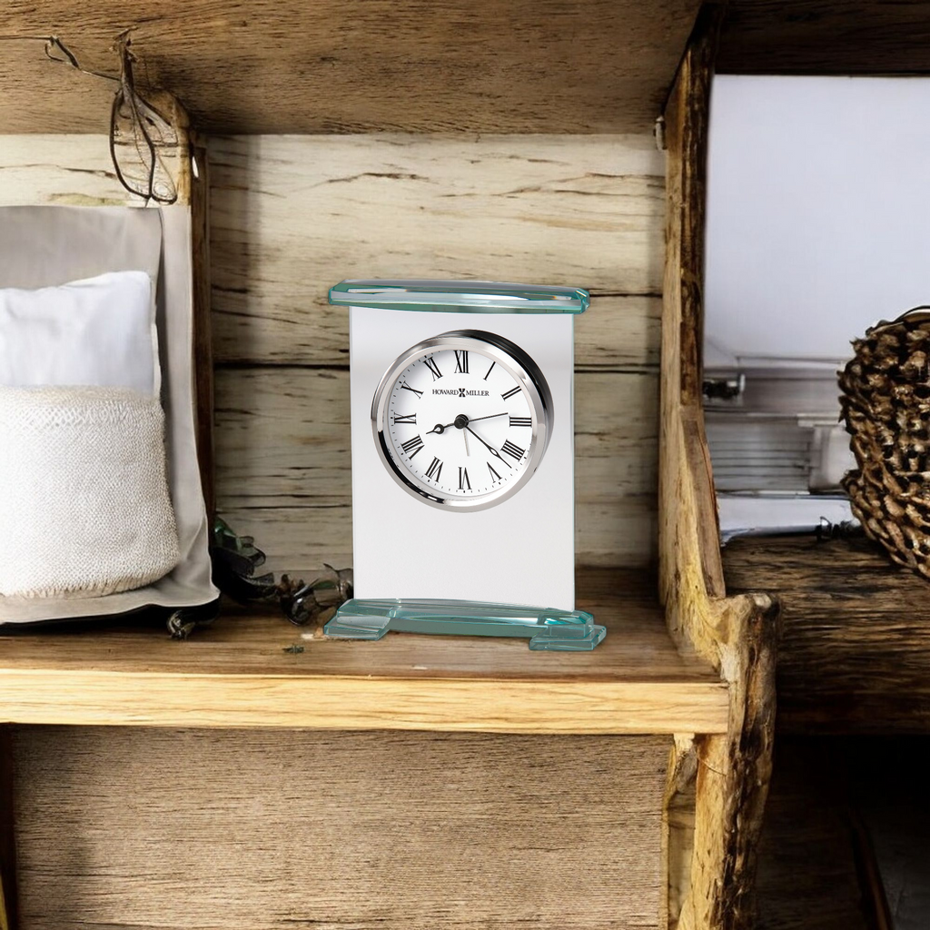 A modern clock on a wooden shelf surrounded by decorative items.