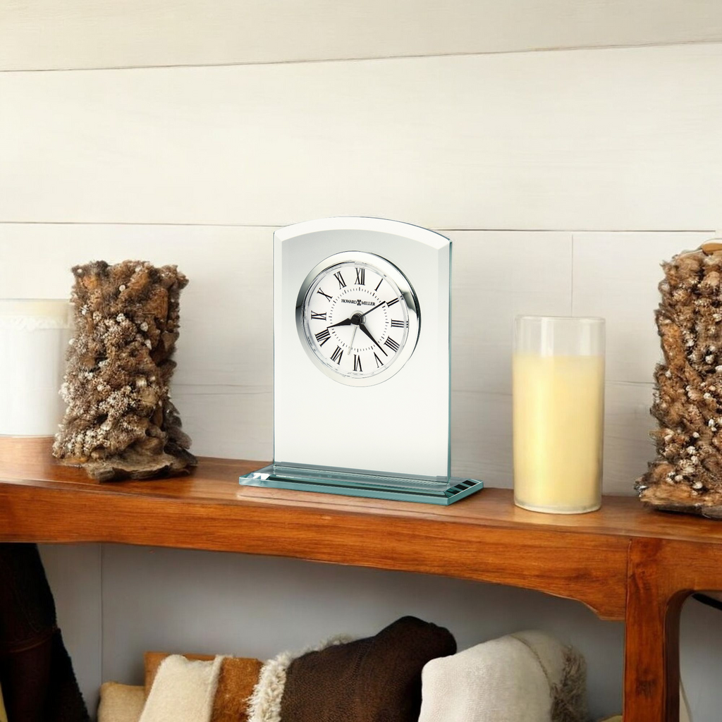 A modern clock on a wooden shelf surrounded by decorative items.