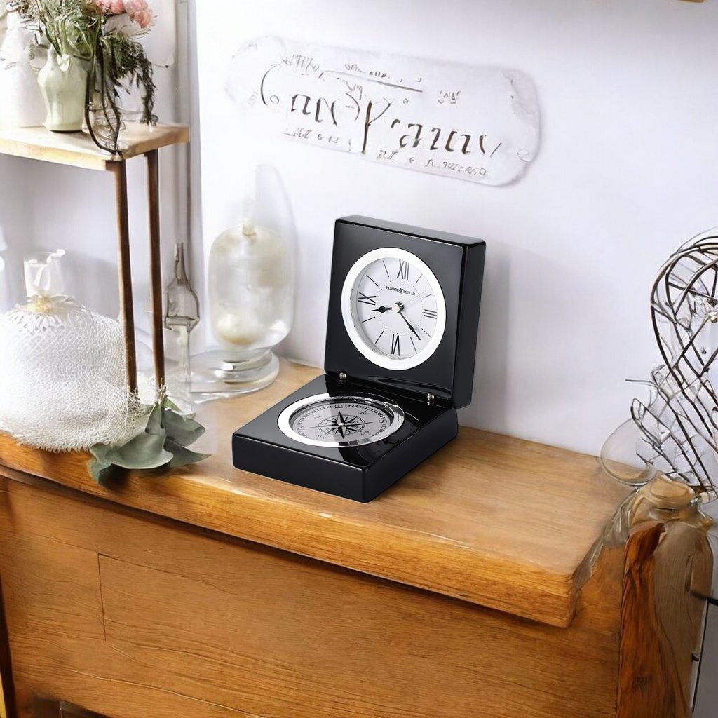 A stylish black desk clock displayed on a wooden table with decorative items in the background.