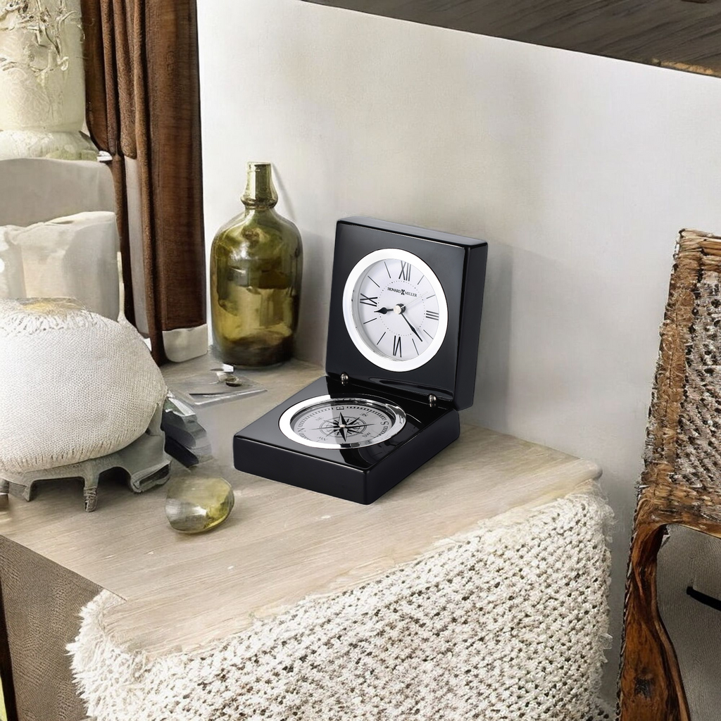 A stylish black clock placed on a wooden table with decorative items.