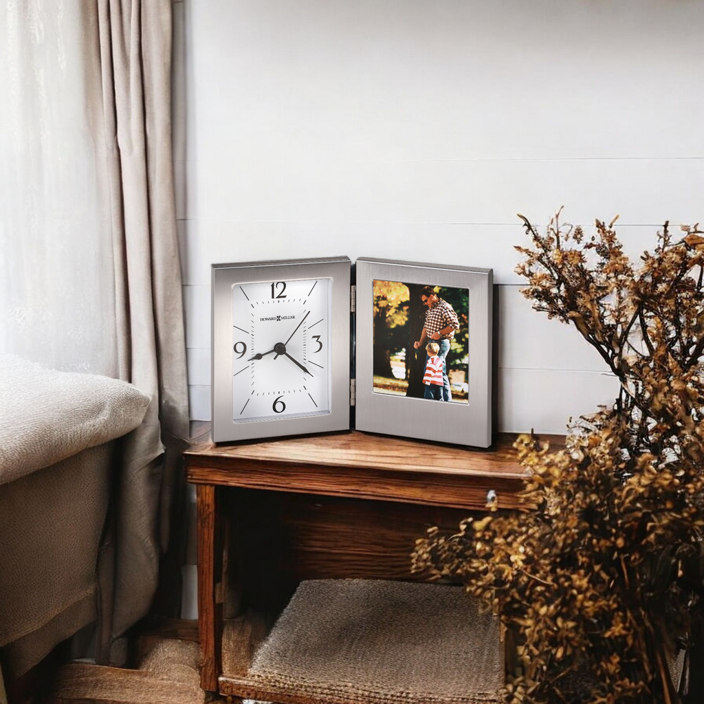 A decorative corner featuring a clock and a framed photo on a wooden table beside a plant.