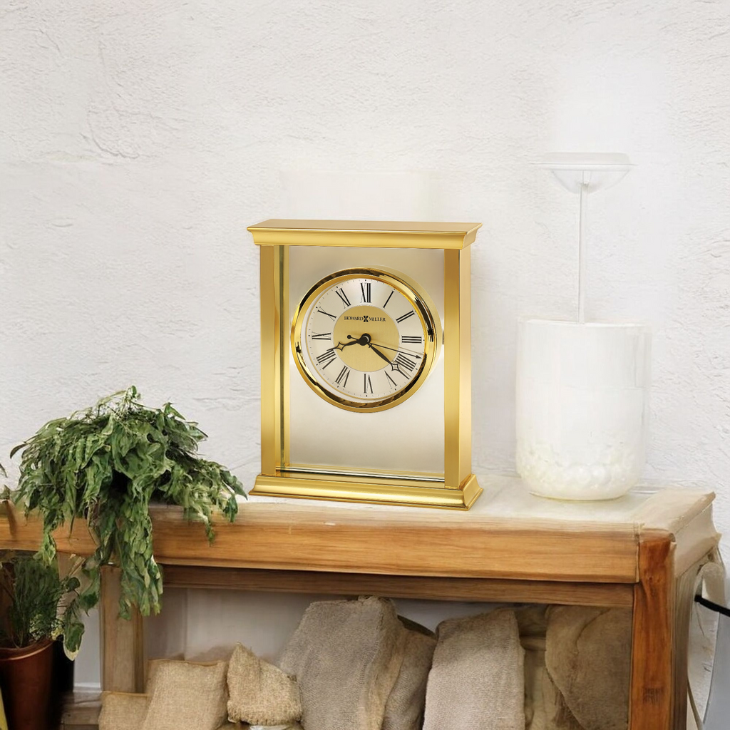A vintage-style gold clock on a wooden shelf next to a white vase and green plants.