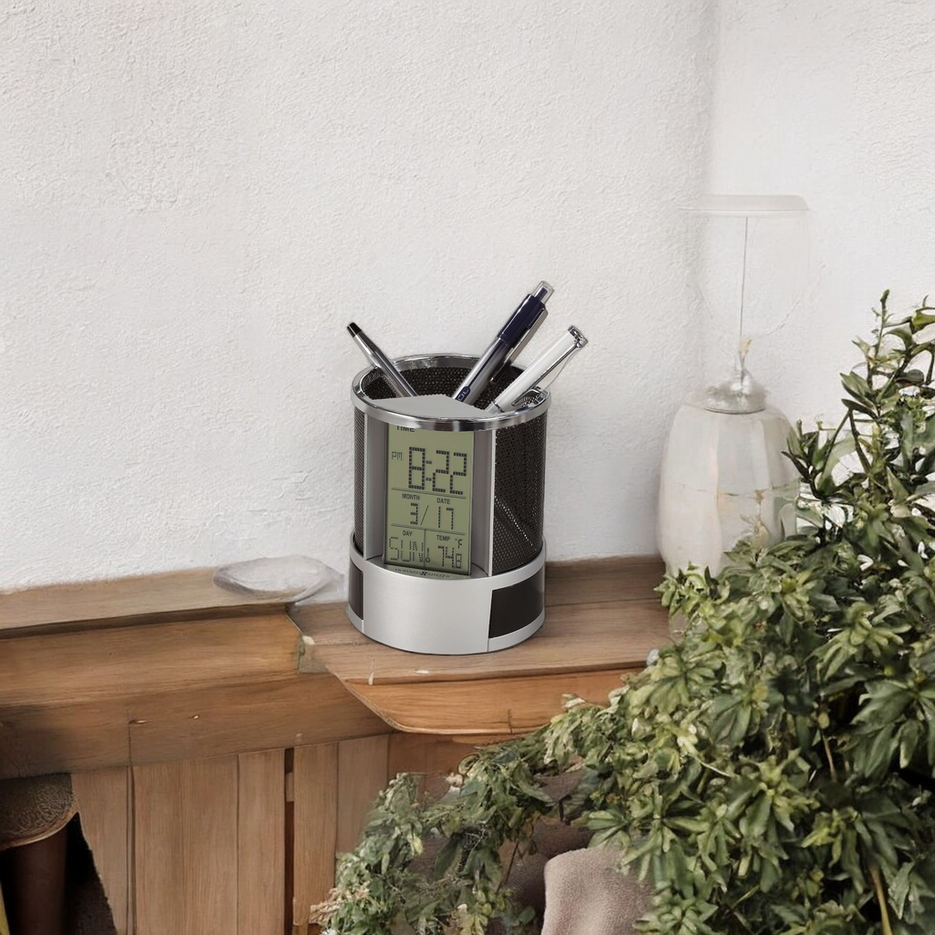 A modern desk organizer with a digital clock and various pens, placed on a wooden surface near a potted plant.