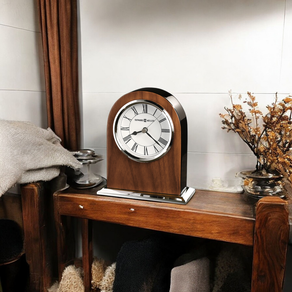 A wooden mantel clock on a shelf with decorative items and a cozy textile.