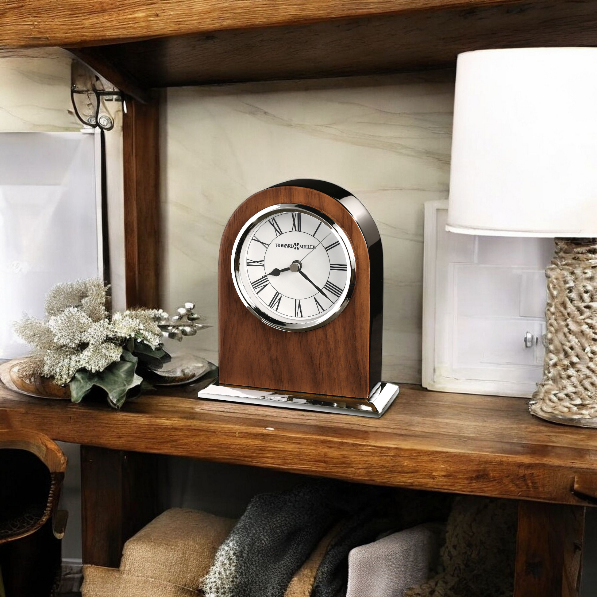 Wooden mantel clock on a shelf next to decorative plants and a lamp
