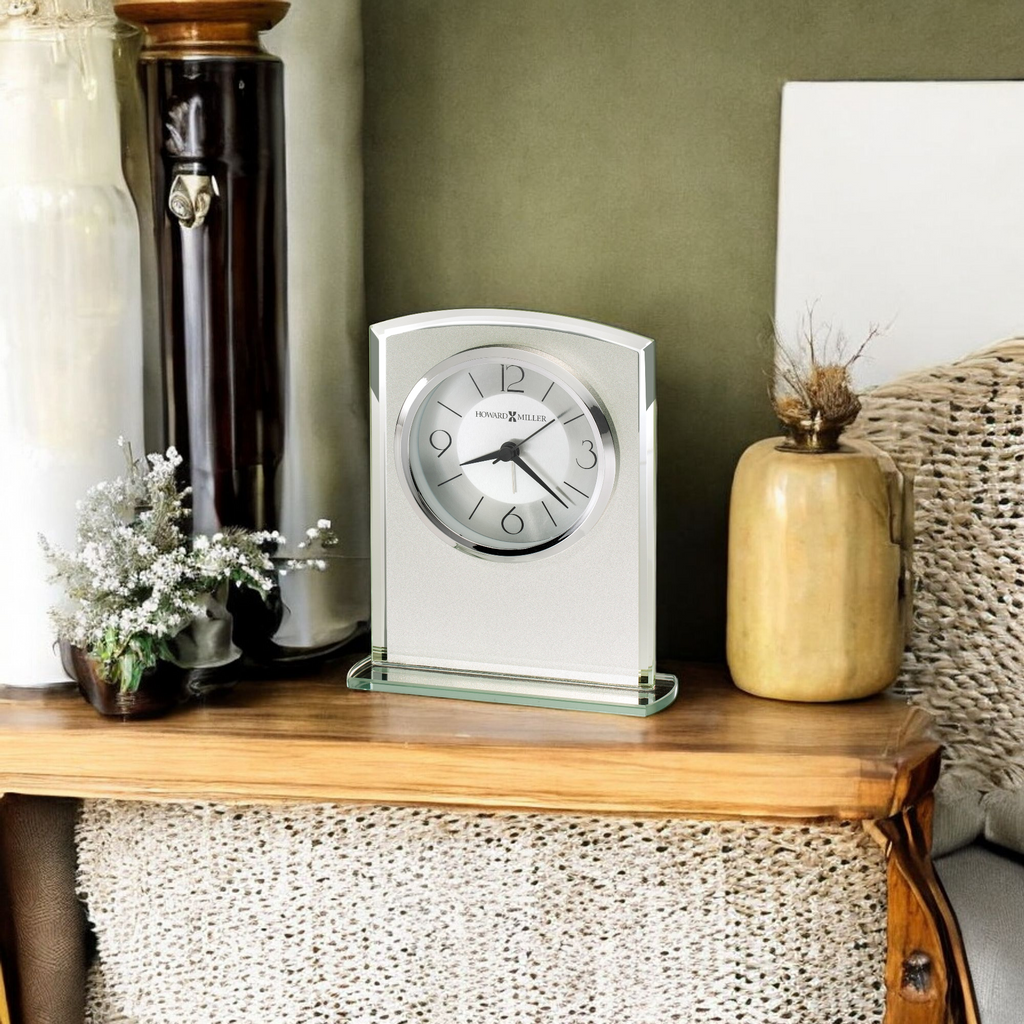 A modern glass clock on a wooden table with decorative items.