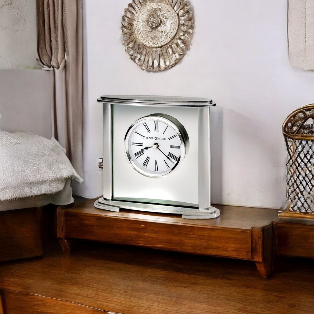 A stylish silver clock on a wooden bedside table in a cozy bedroom setting.