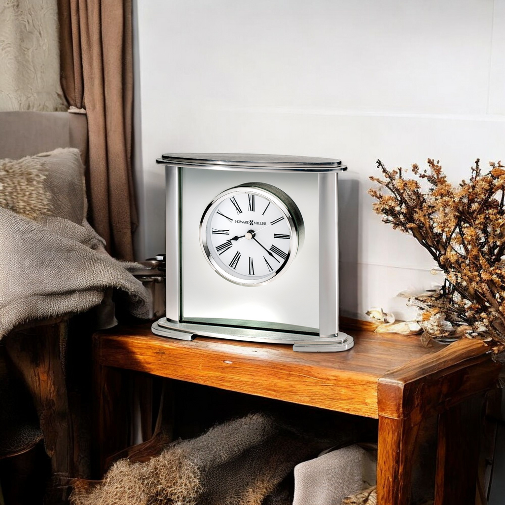 A modern tabletop clock placed on a wooden table next to a cozy blanket and decorative branches.