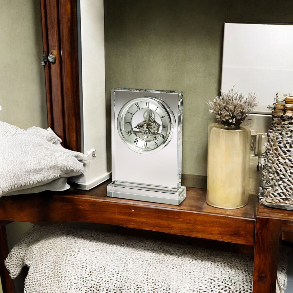 A decorative clock displayed on a wooden shelf alongside vases and soft textiles.