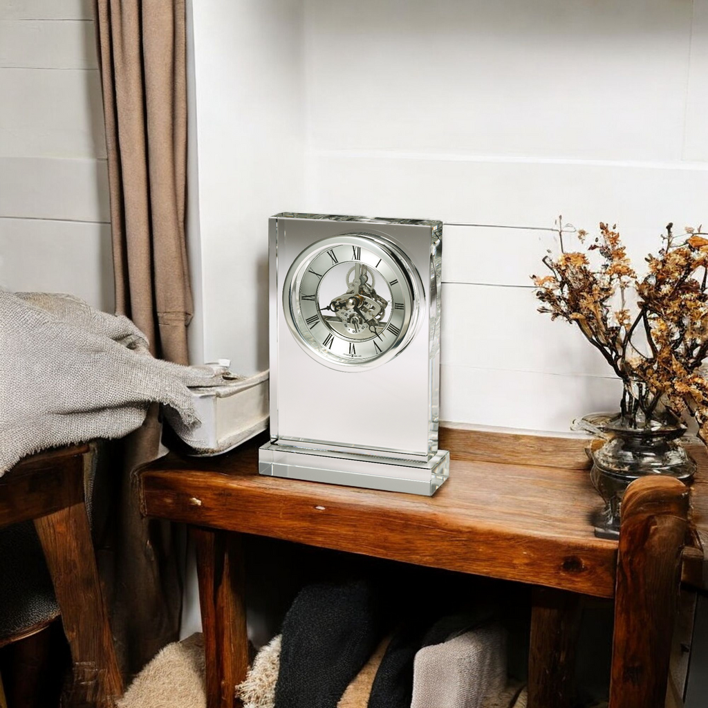 A stylish clock on a wooden table next to a cozy blanket and decorative plant.