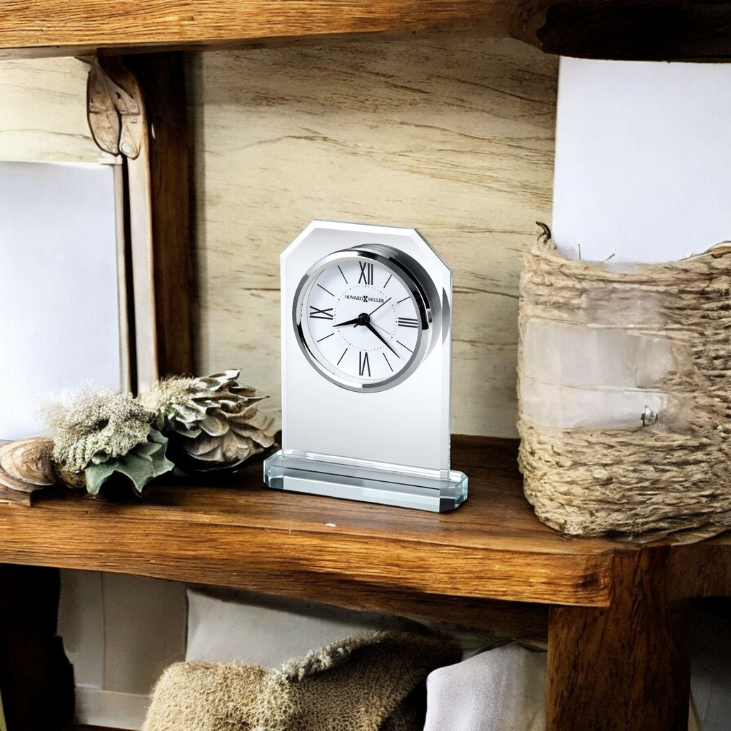 A decorative clock with a silver finish displayed on a wooden shelf among natural decor items.